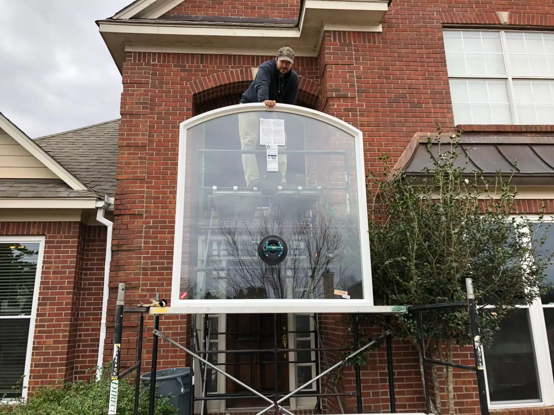 Installer replacing a large arched window on a two-story brick home in Jackson, Mississippi